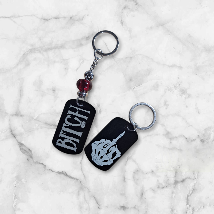 Black anodized aluminum dog tag
engraved with Bitch on one side
and the middle finger skeleton hand on the other.