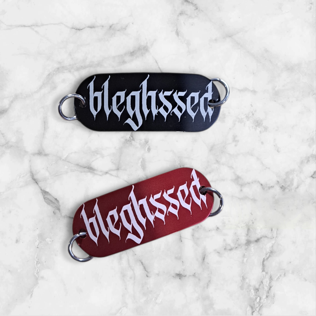 Bent aluminum lacing tag with bleghssed engraved on it. Available in Black or Red