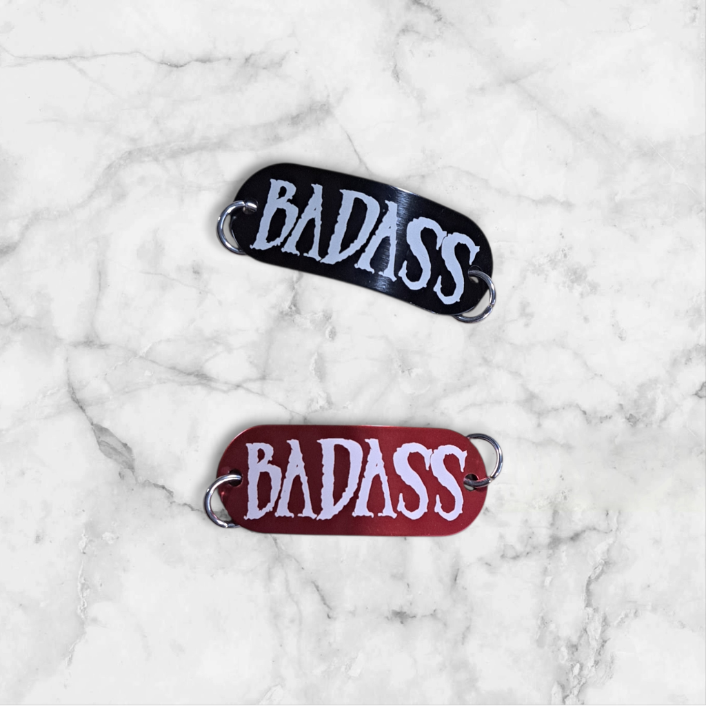 Bent aluminum lacing tag with Badass engraved on it. Available in Black or Red.