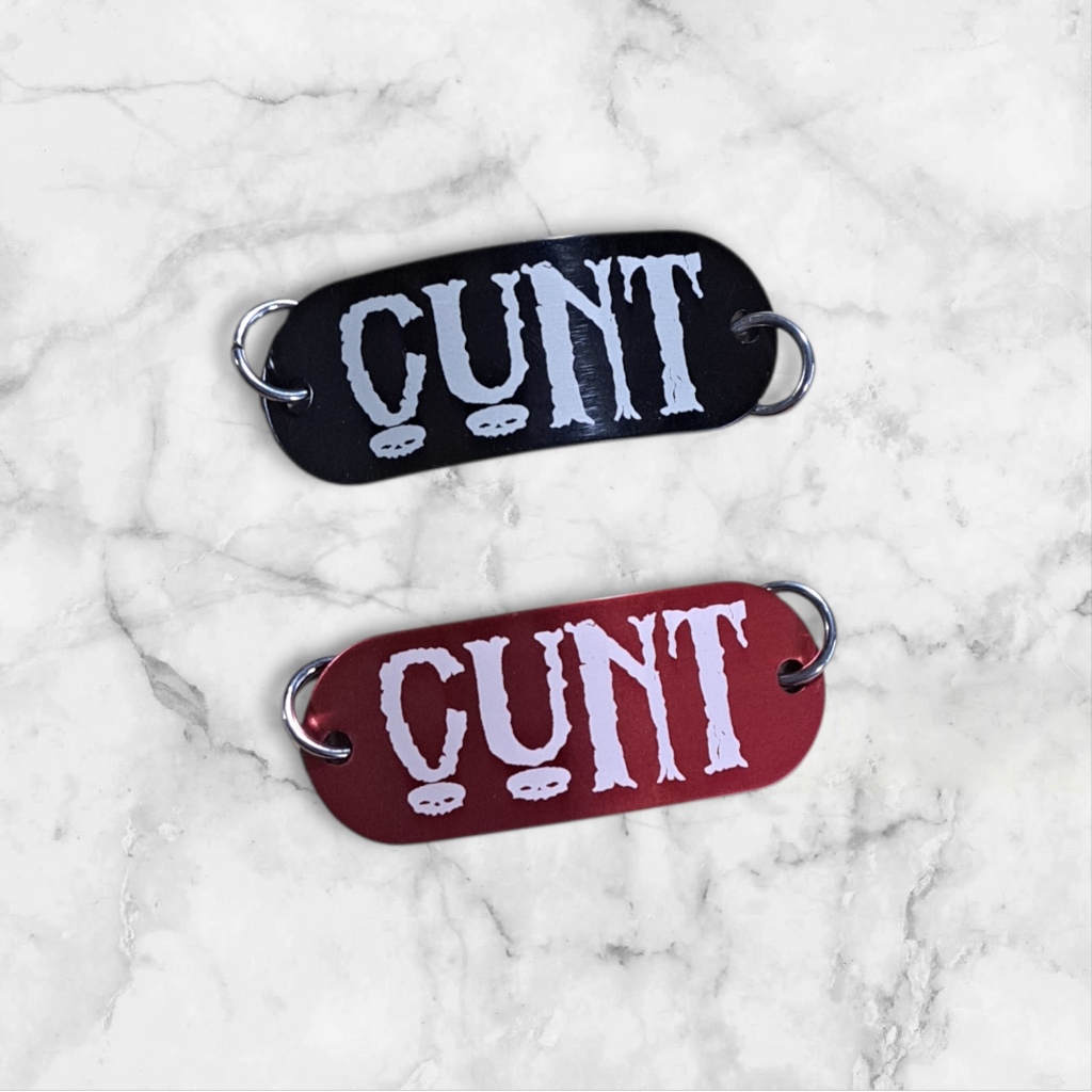 Bent aluminum lacing tag with CUNT engraved on it. Available in Black or Red
