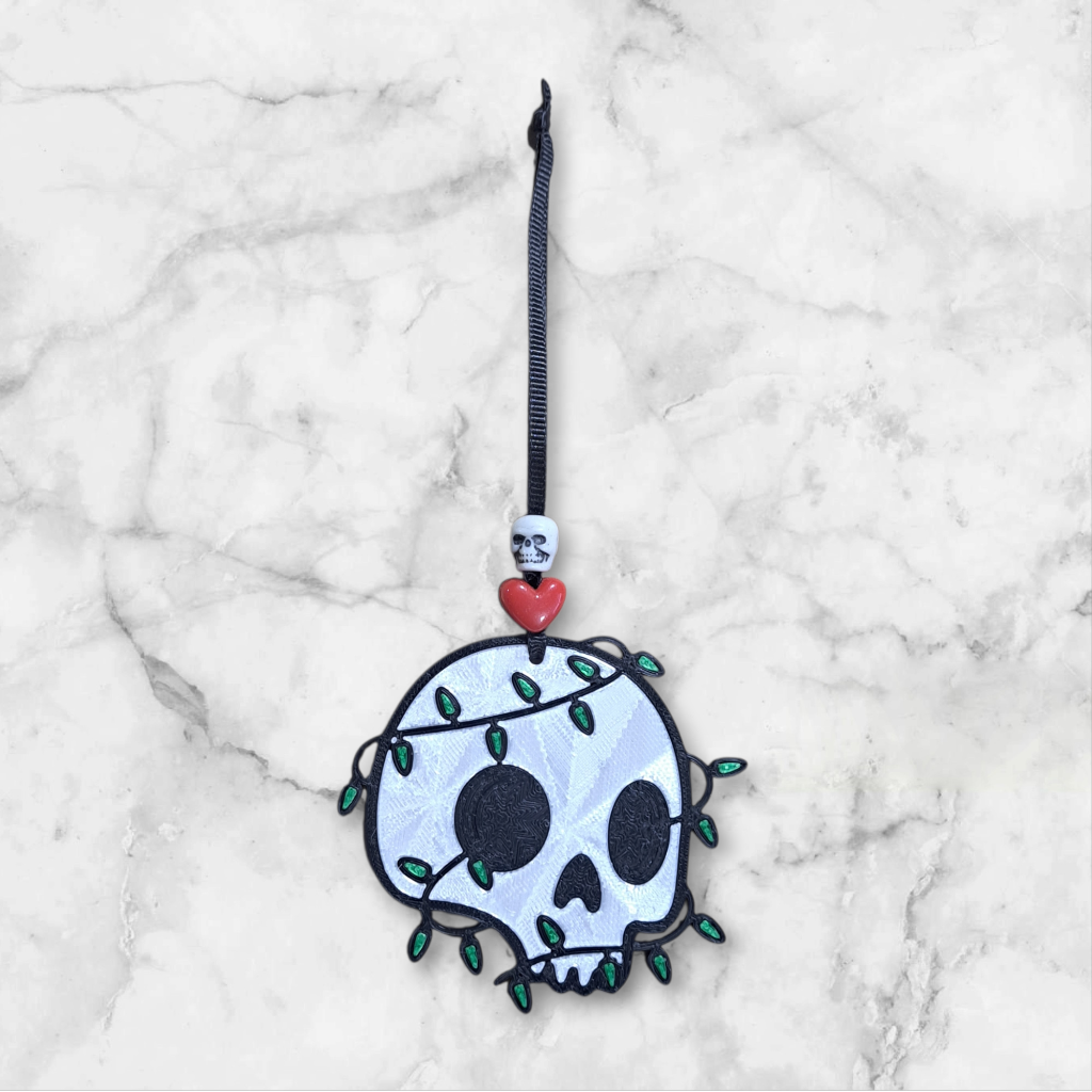 Skull ornament tangled with a string of green Christmas lights, beaded with a heart and skull ribbon hanger
